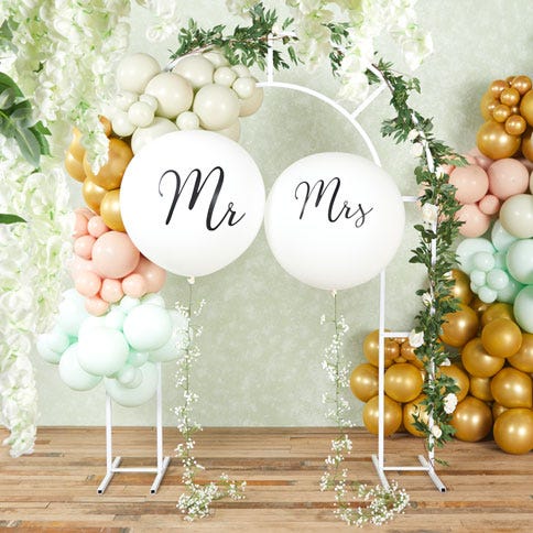 Large round and white Mr & Mrs balloons with a pastel balloon arch in the background